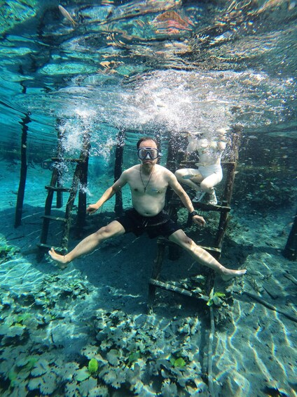 A person underwater, sitting on a wooden structure, surrounded by marine life. 5