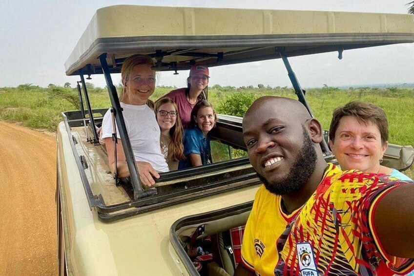 A group of people in a safari vehicle on a dirt road with grassy fields in the background. 3