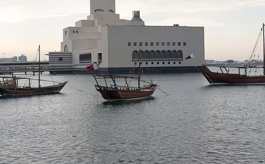 Three traditional wooden boats anchored near a modern white building with a flag. 3