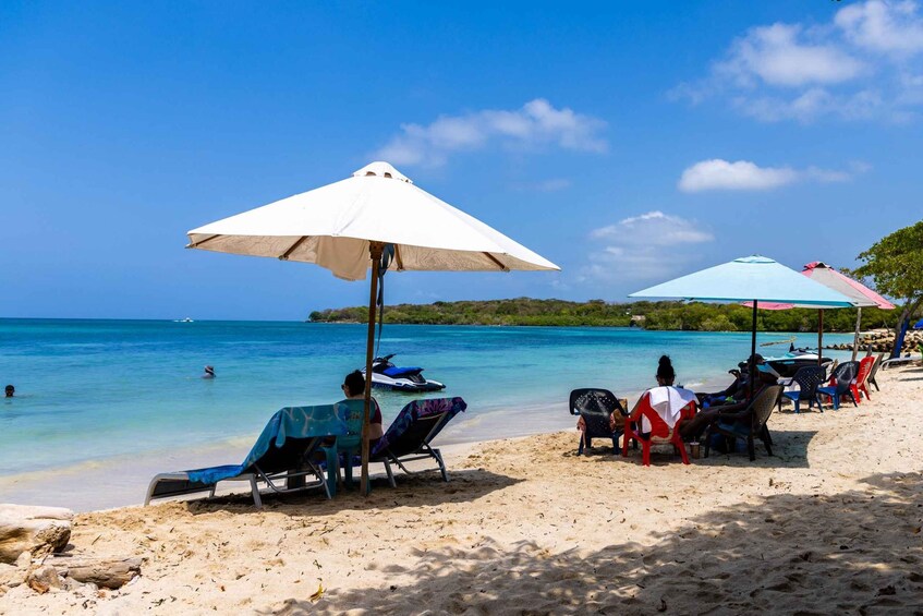 Una playa con gente relajándose bajo sombrillas, un jet ski en el agua y cielos azules despejados. 1