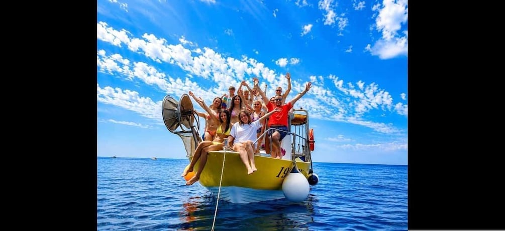 A group of people on a yellow boat with a white sail, floating on the ocean. 3