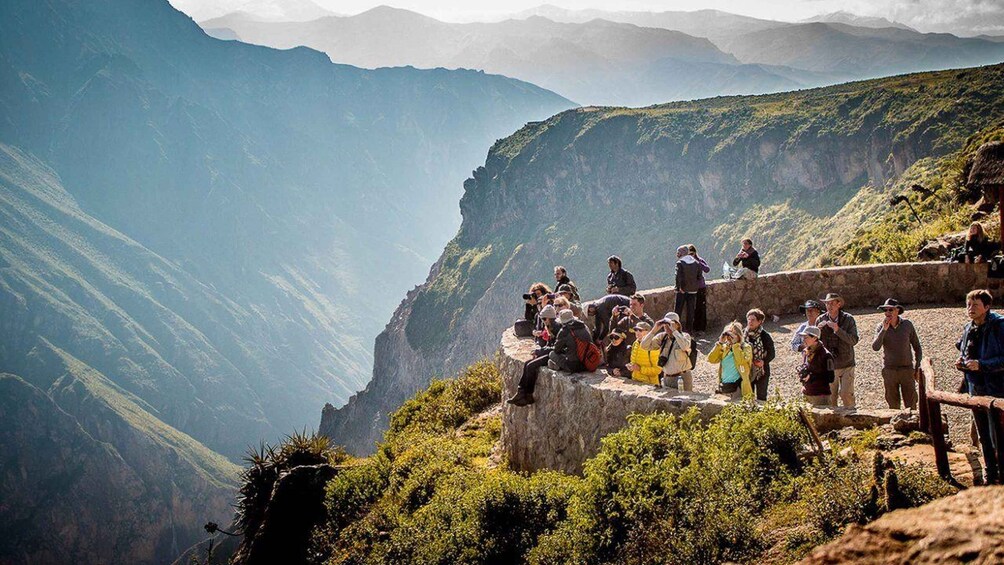 A group of people on a mountain trail with a view of a deep valley and distant mountains. 5