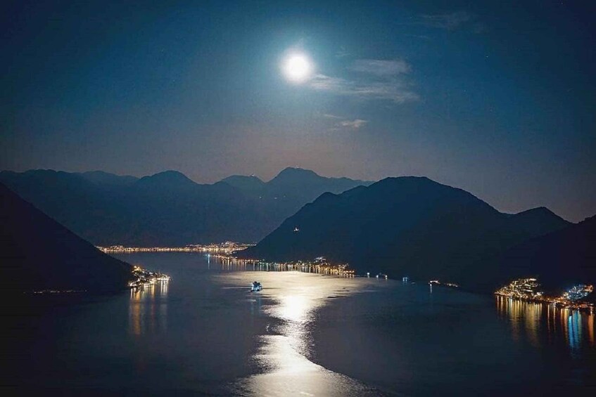 A nighttime lake with a boat and distant city lights. 1