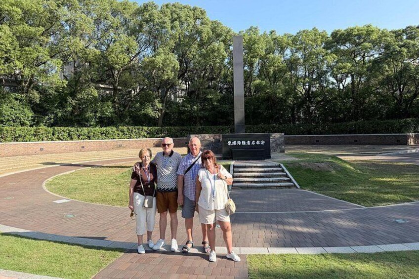 A group of people standing in a park with a monument and a brick pathway. 2
