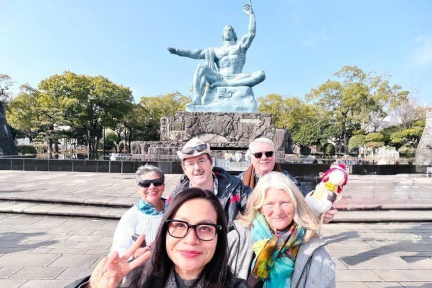 A group of people posing in front of a statue with a rocky base and trees in the background. 1