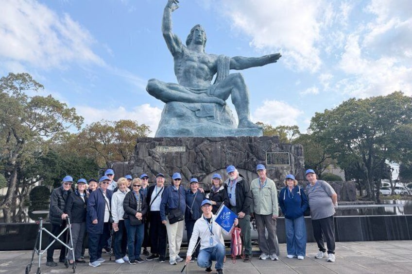 A group of people posing in front of a bronze statue of a seated figure with outstretched arms. 4