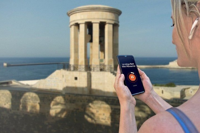 Una persona sostiene un teléfono inteligente con una interfaz de aplicación, observando un monumento histórico junto al mar. 5