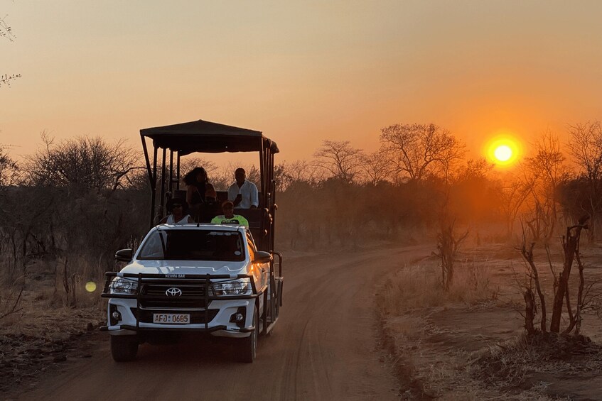 A white SUV with a roofed trailer driving on a dirt road during sunset. 2