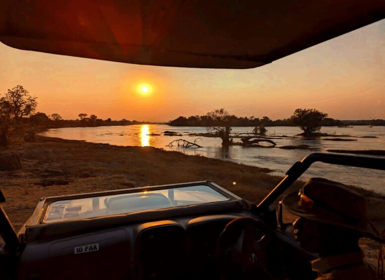 A sunset over a river with trees and a vehicle in the foreground. 5