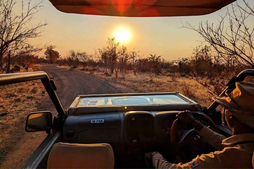 A vehicle driving on a dirt road with a sunset in the background. 1