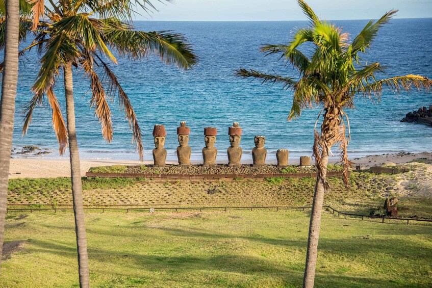 A beach with a row of Moai statues, palm trees, and the ocean. 4