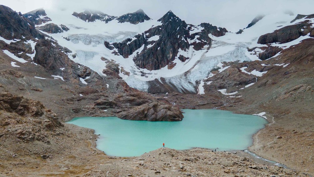A turquoise lake surrounded by rugged mountains with snow patches. 1