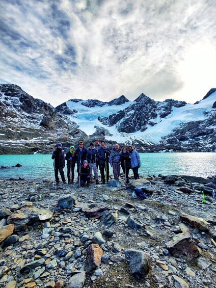 A group of people standing on a rocky shore with a glacier and mountains in the background. 4
