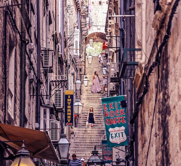 A narrow street with buildings, a staircase, and signs for 'Hugo Internet' and 'Exit Rock Cafe'. 3