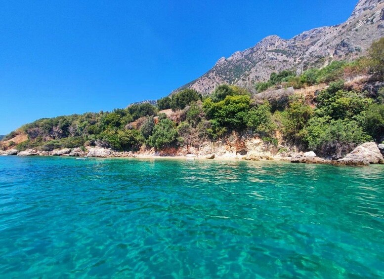 A coastal landscape with clear turquoise waters, rocky cliffs, and dense greenery. 2