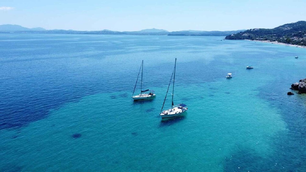 A coastal area with clear blue waters, several sailboats anchored, and a distant shoreline with buildings. 5