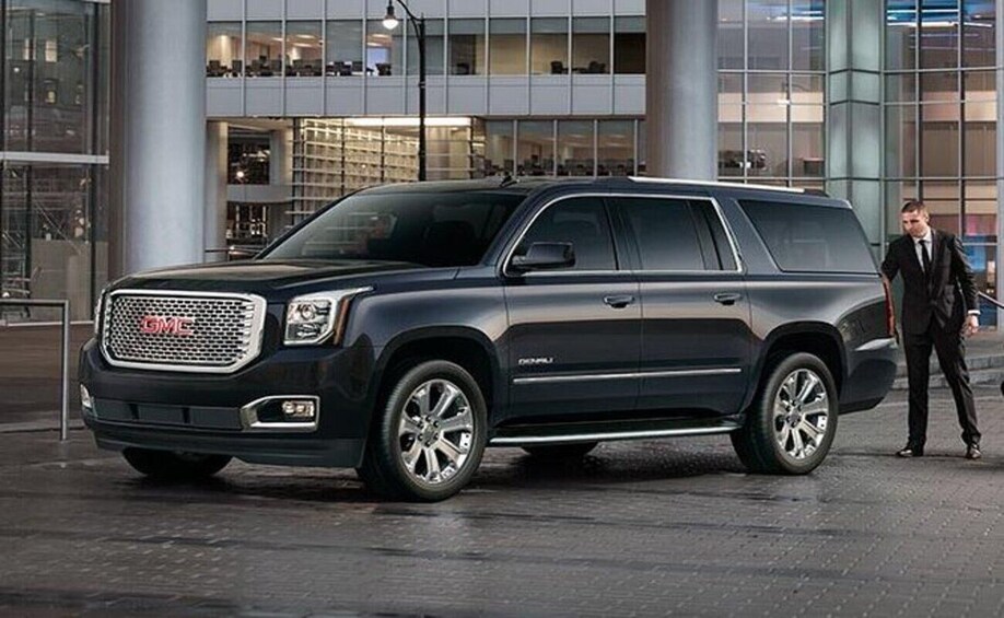 A GMC Yukon SUV parked in front of a modern building. 3