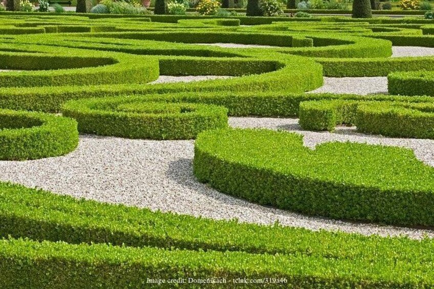 Een verzorgde tuin met geometrische haagdoolhoven en grindpaden. 4