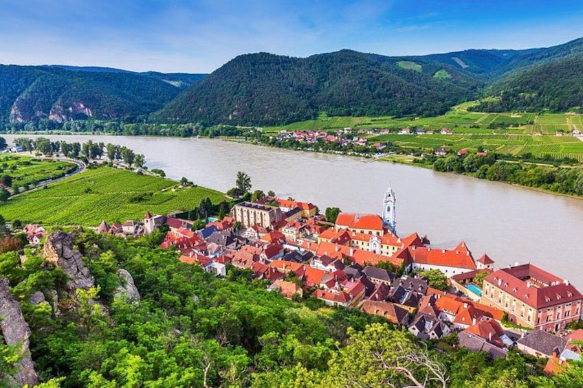 A river flowing through a town with red-roofed buildings and green hills in the background. 4