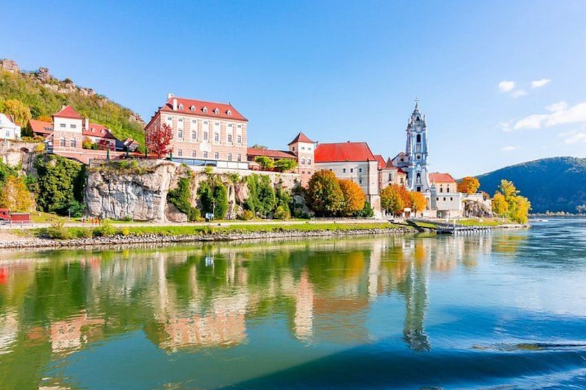 A river with buildings on a hillside, a church, and autumn-colored trees. 2