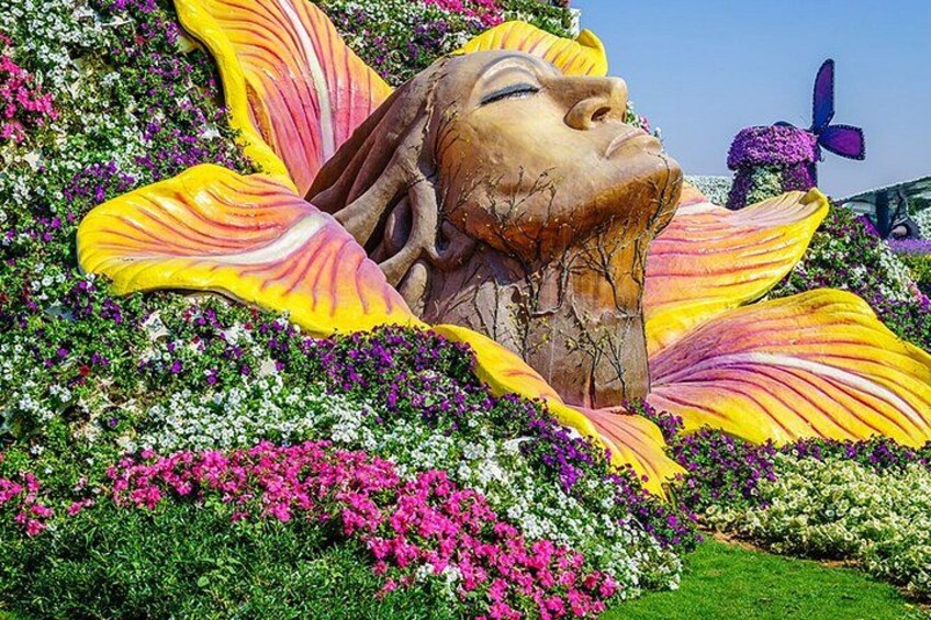 A large floral sculpture with a woman's face, surrounded by colorful flowers and greenery. 1