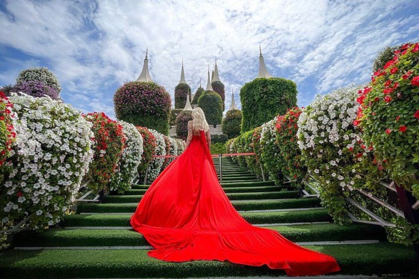 A woman in a red dress walking down a staircase surrounded by lush greenery and white flowers. 2