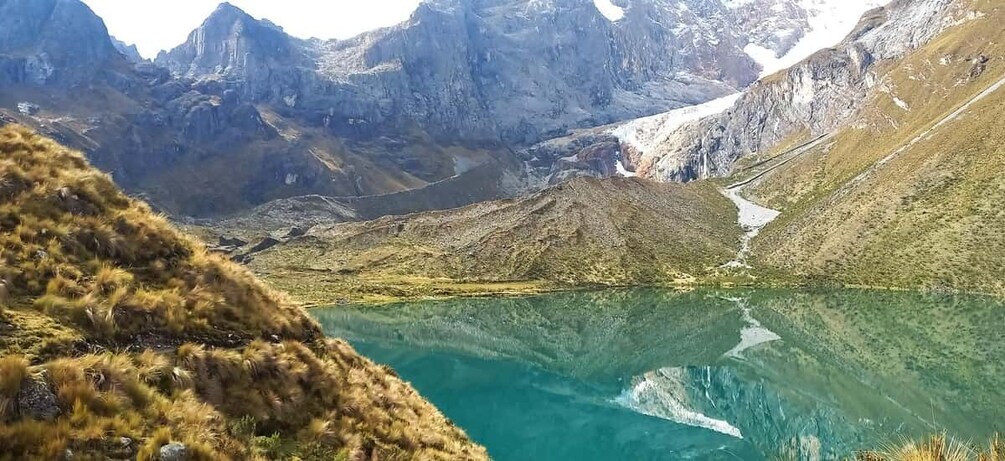 A mountain lake with clear turquoise water, surrounded by rugged terrain and sparse vegetation. 1