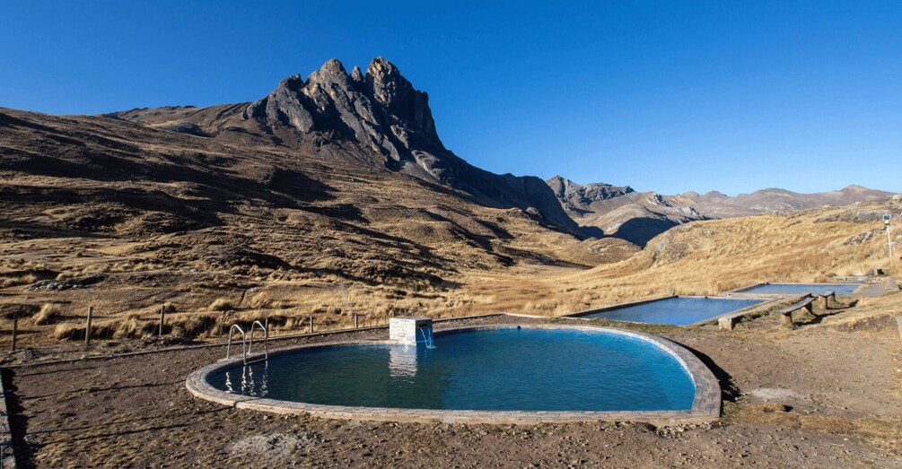 A swimming pool surrounded by dry, hilly terrain with a prominent mountain in the background. 2