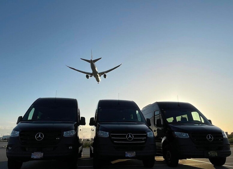 Three Mercedes-Benz vans parked in a row with an airplane flying overhead. 1