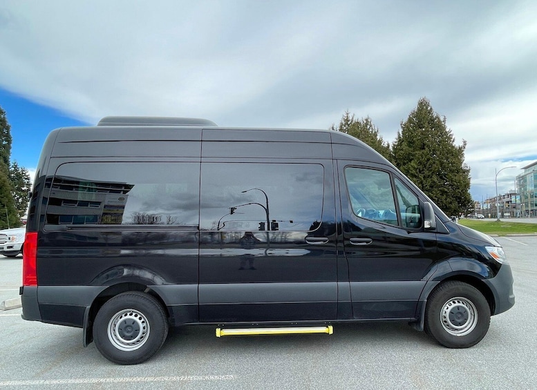 A black van parked in a lot with a yellow barrier in front. 2