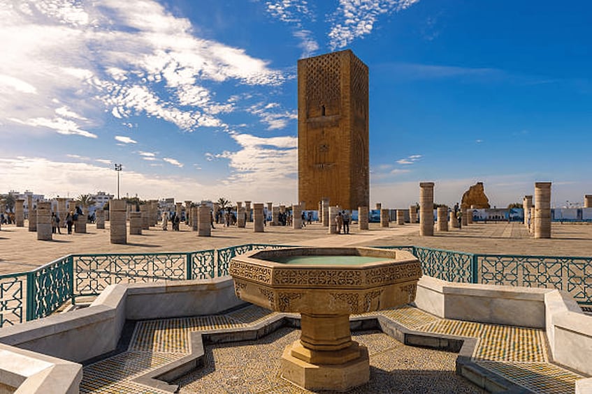 A historical square with a prominent tower, patterned fountain, and traditional architecture. 3