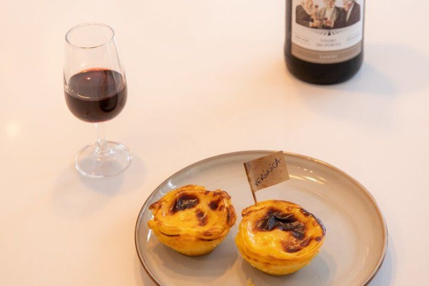 Two Portuguese egg tarts on a plate with a tag, a glass of red wine, and a bottle of wine in the background. 3