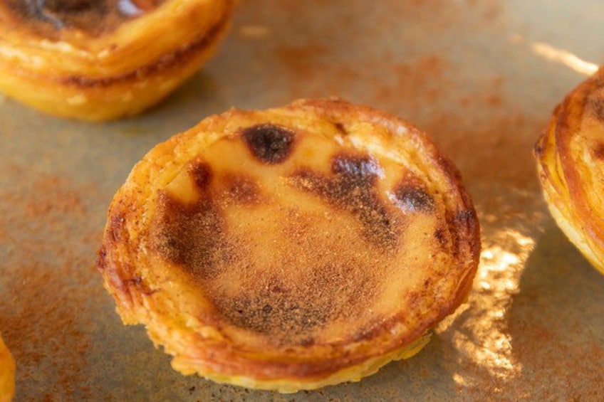 A close-up of a Portuguese custard tart with a golden-brown crust and a slightly charred top. 4