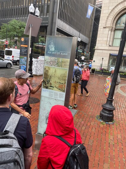 A group of people near a historical marker with a map and information about the Old State House in Boston. 1