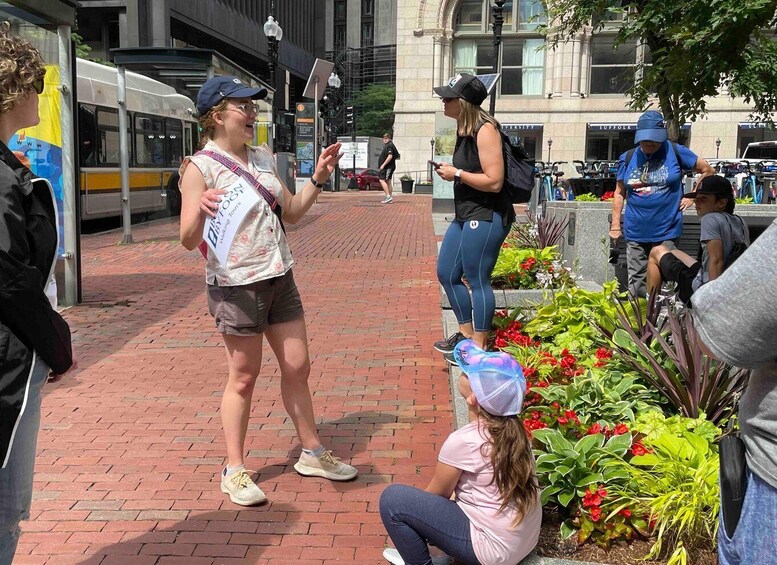 A woman in a pink shirt and blue cap sitting on the ground, talking to another woman in a black shirt and blue cap. 5