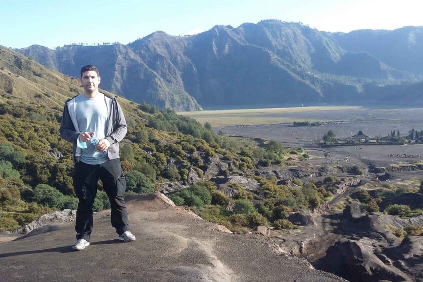 A person standing on a rocky outcrop with a mountainous landscape in the background. 2