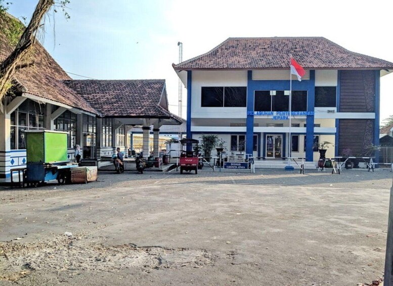 A building with a tiled roof and a flag, a covered area with a green container, and a paved ground. 3