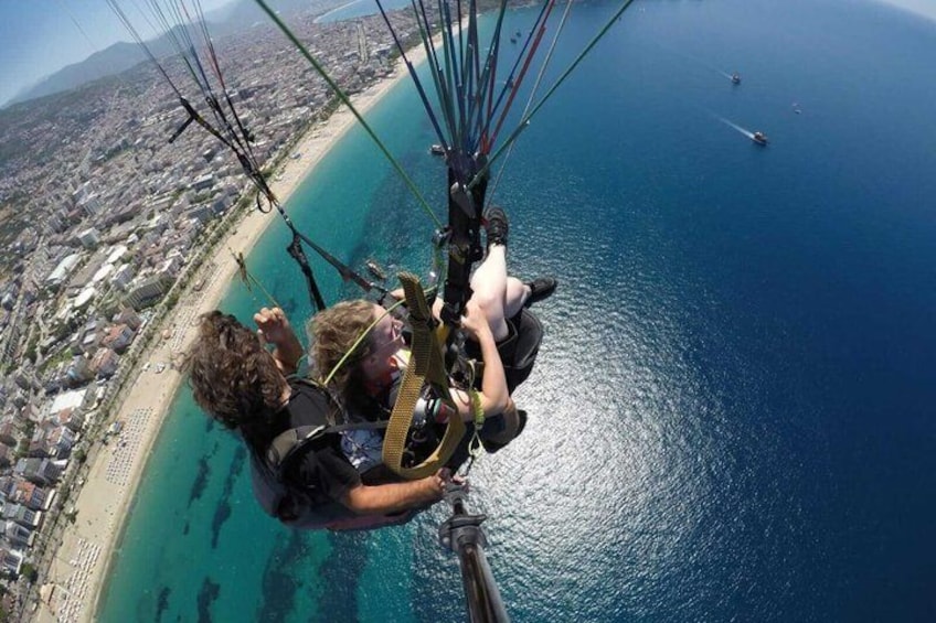En tandem-paragliding aktivitet over et kystområde med en strand og klart, blåt vand. 5