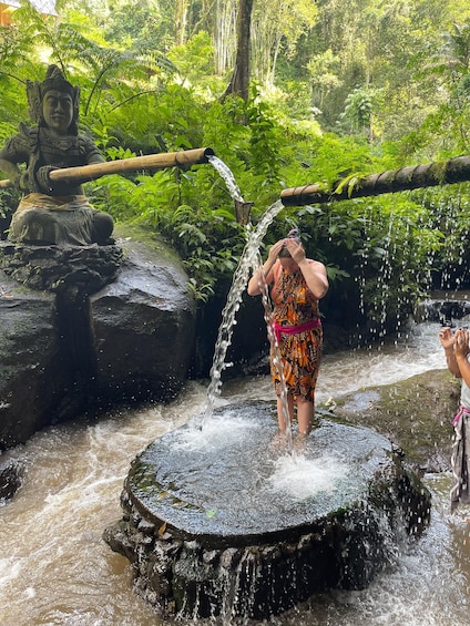 A person bathing in a natural water feature surrounded by lush greenery and a statue. 5