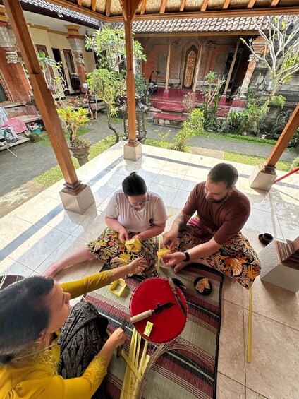 Three people sitting on a mat, engaged in a traditional activity with wooden blocks and a red bowl. 3