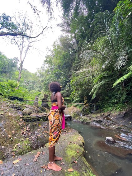 A woman standing on a rock by a stream in a forest. 4