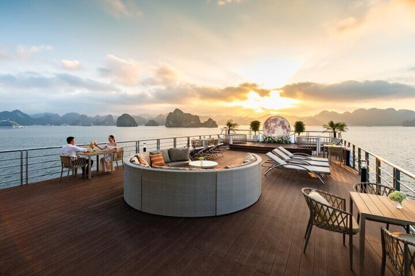 Une terrasse dotée d’un espace salon circulaire, d’une table et de chaises, offrant une vue sur une étendue d’eau avec des montagnes en arrière-plan. 2