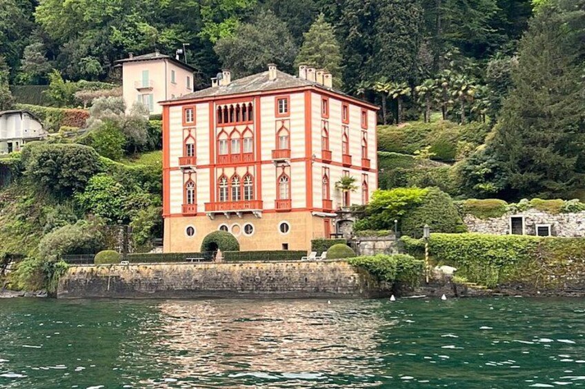 A red and yellow building with arched windows, surrounded by lush greenery and a body of water. 3