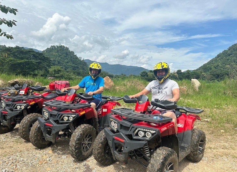 Two people on ATVs in a rural setting with mountains in the background. 1