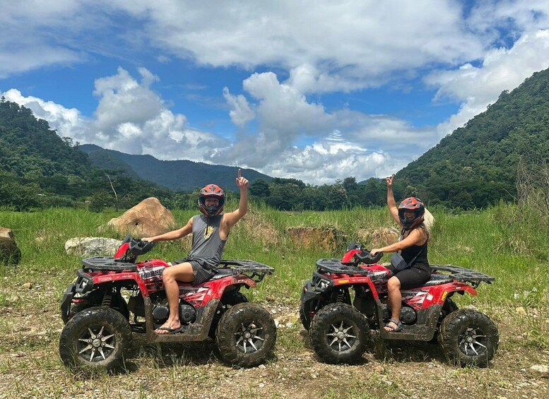 Two people on red ATVs in a grassy field with mountains in the background. 4