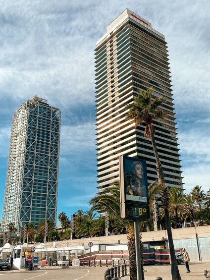 Two tall buildings, one with a grid-like facade and the other with horizontal lines, palm trees, and a pedestrian crossing. 4