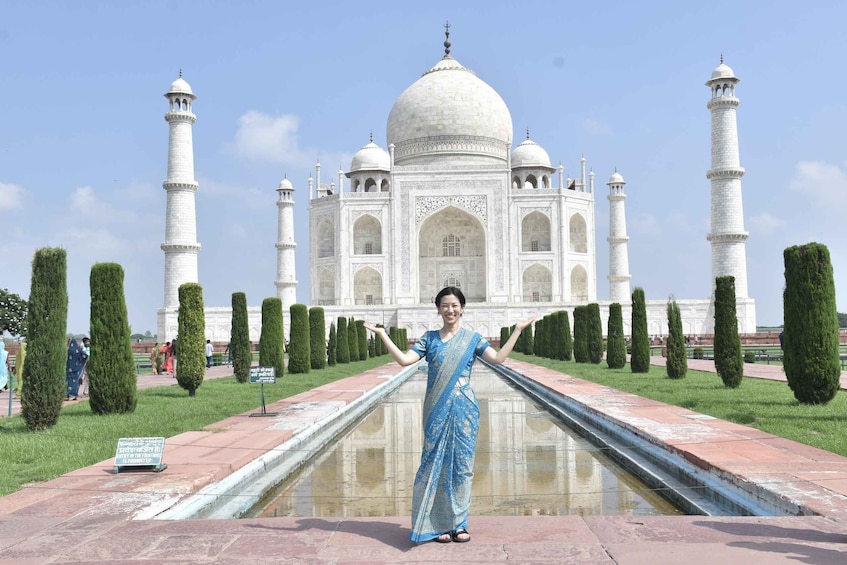 En person i en blå sari som står framför Taj Mahal, och vars spegelbild syns i vattnet. 2