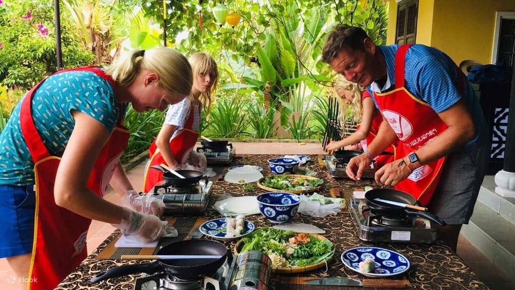 A group of people preparing food outdoors with a table full of dishes and cooking utensils. 3
