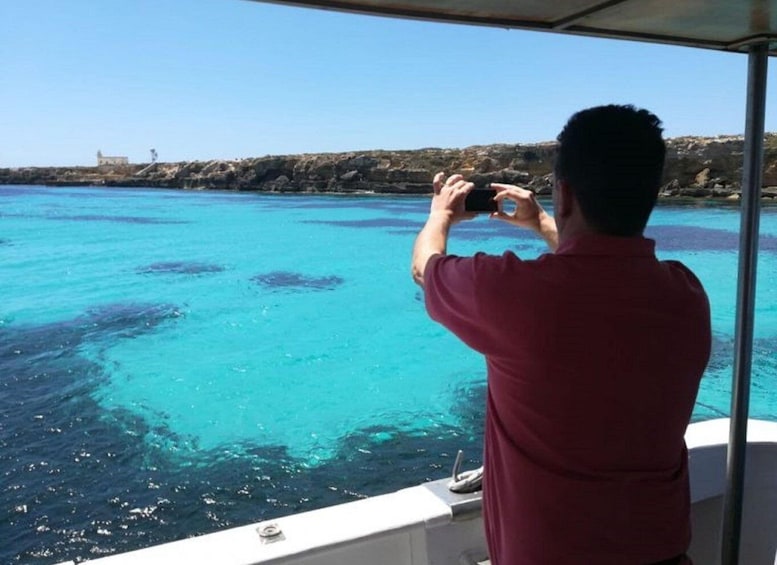 A person taking a photo of a boat with clear blue water and rocky coastline. 3