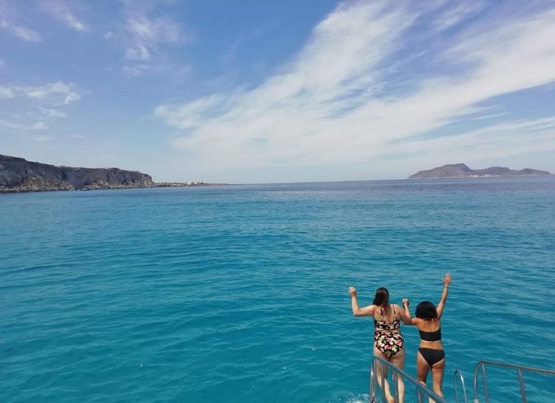 Two people at the edge of a boat, overlooking a turquoise sea with distant landforms. 4